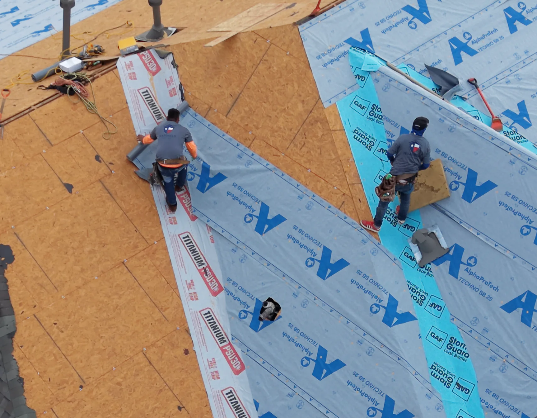 Roofing crew installing blue underlayment over exposed roof decking.