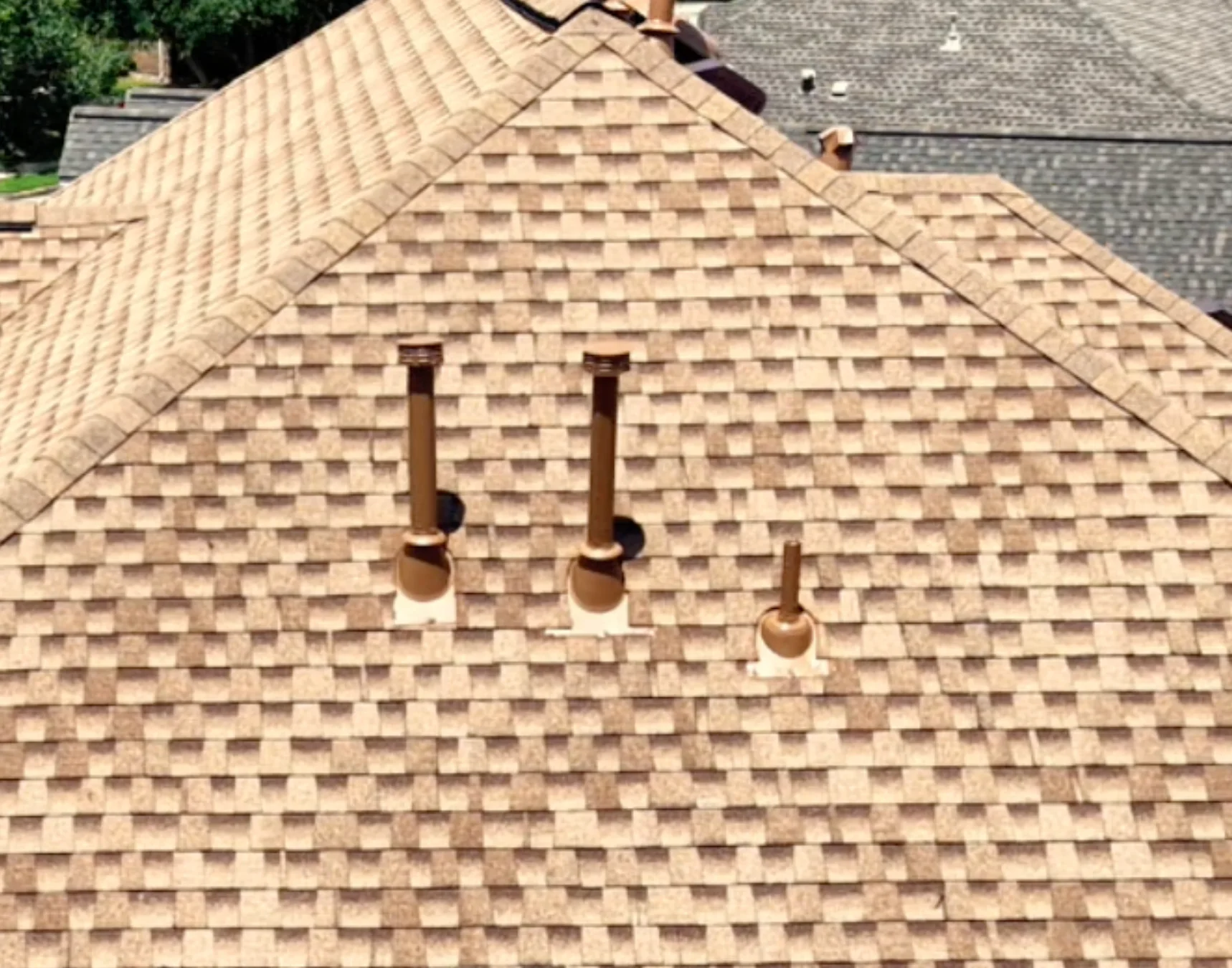Aerial close view of sealed and painted roof vents on a light brown shingle roof.