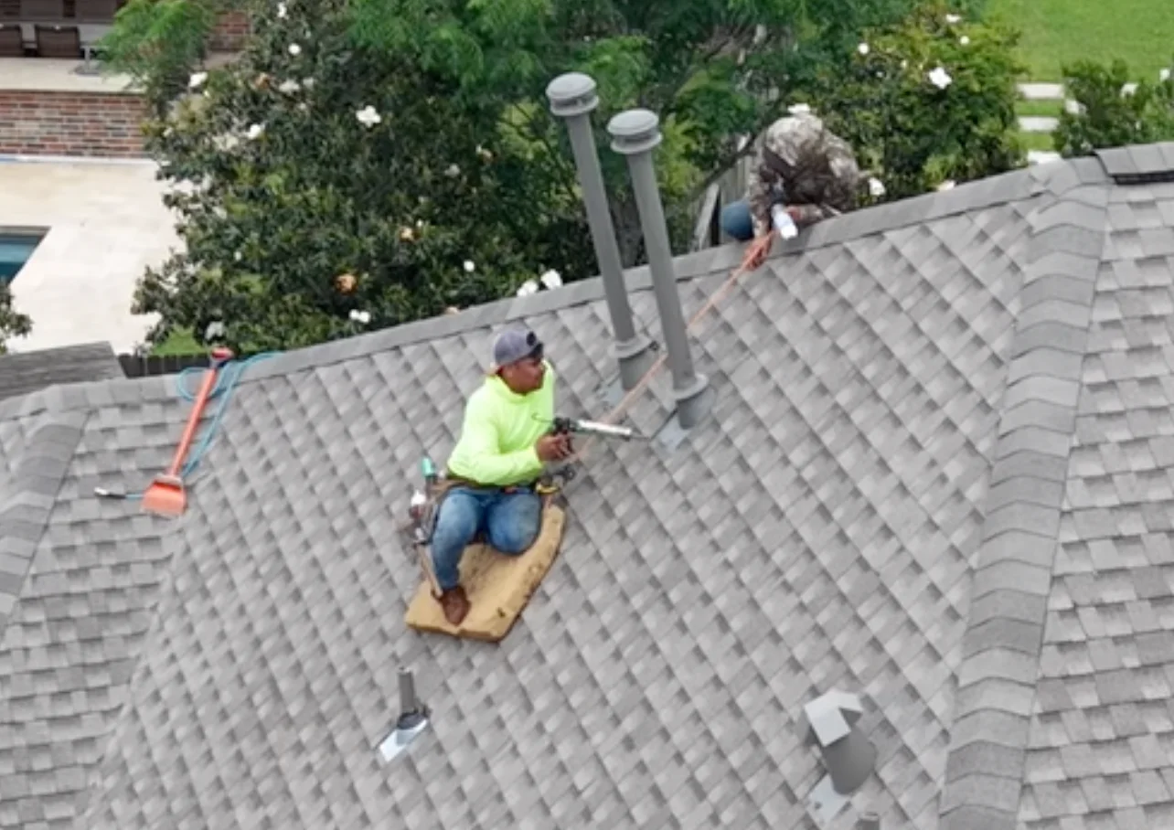 Roofing crew working around several vents on a gray shingle roof.
